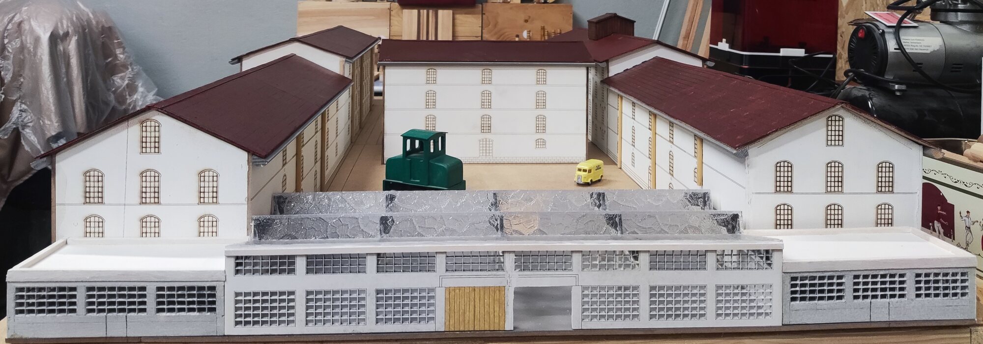 Vue frontale de la maquette achevée : la halle vitrée au premier plan, la cour en U et les trois corps de bâtiment aux toitures bordeaux.